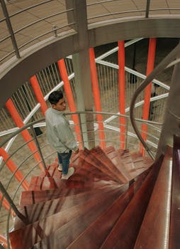 一个穿着牛仔夹克的年轻人正沿着室内带有金属栏杆的当代螺旋楼梯向上走