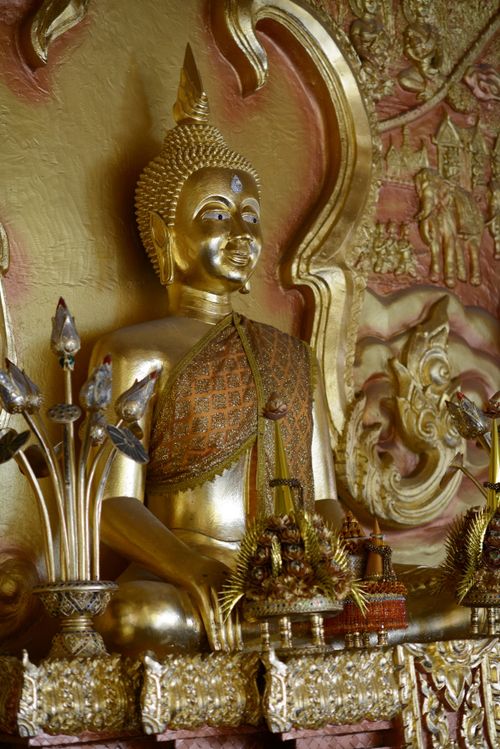 Free A majestic golden Buddha statue surrounded by intricate carvings in a tranquil temple setting. Stock Photo