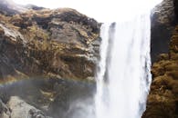 冰岛壮观的瀑布从崎岖的景观中倾泻而下，与一道绚丽的彩虹交相辉映