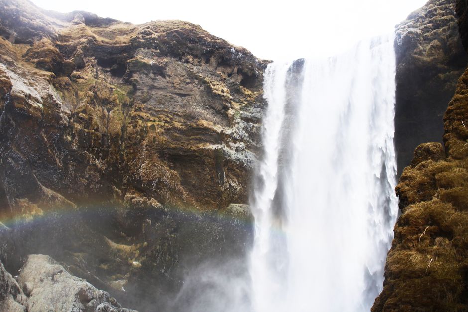 Stunning Icelandic waterfall cascading with a vibrant rainbow in rugged landscape.