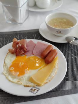 A savory breakfast plate featuring eggs, bacon, ham, cheese, and soup.