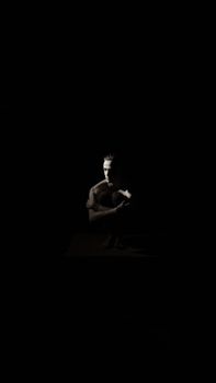 A moody black and white portrait of a shirtless man in a dark studio setting.