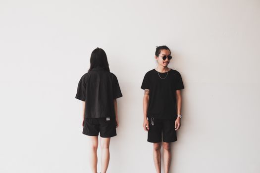 A minimalist photograph of an Asian couple standing against a white wall, showcasing modern fashion.