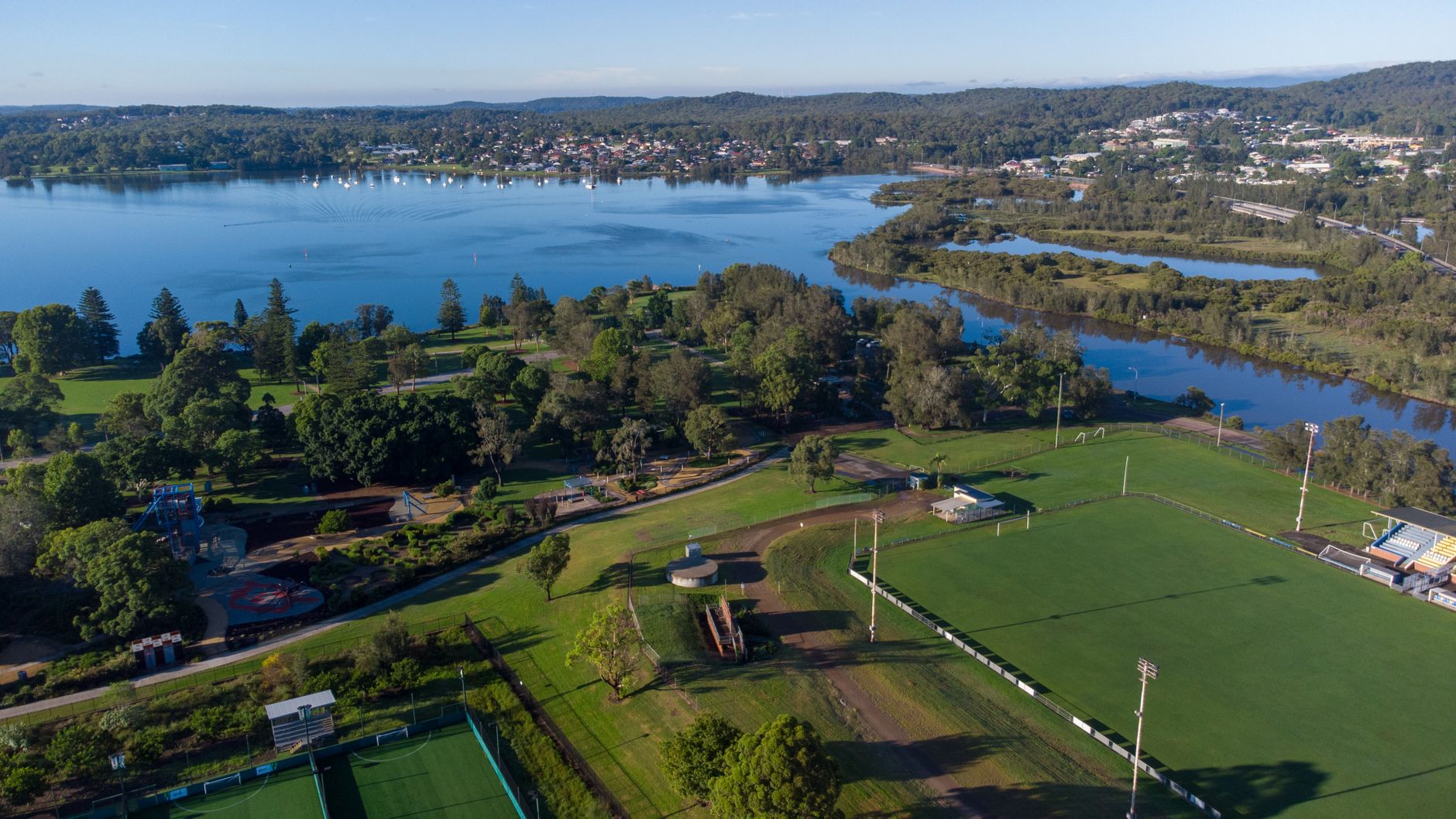 Scenic aerial view of a lush park next to a calm river under a clear sky.