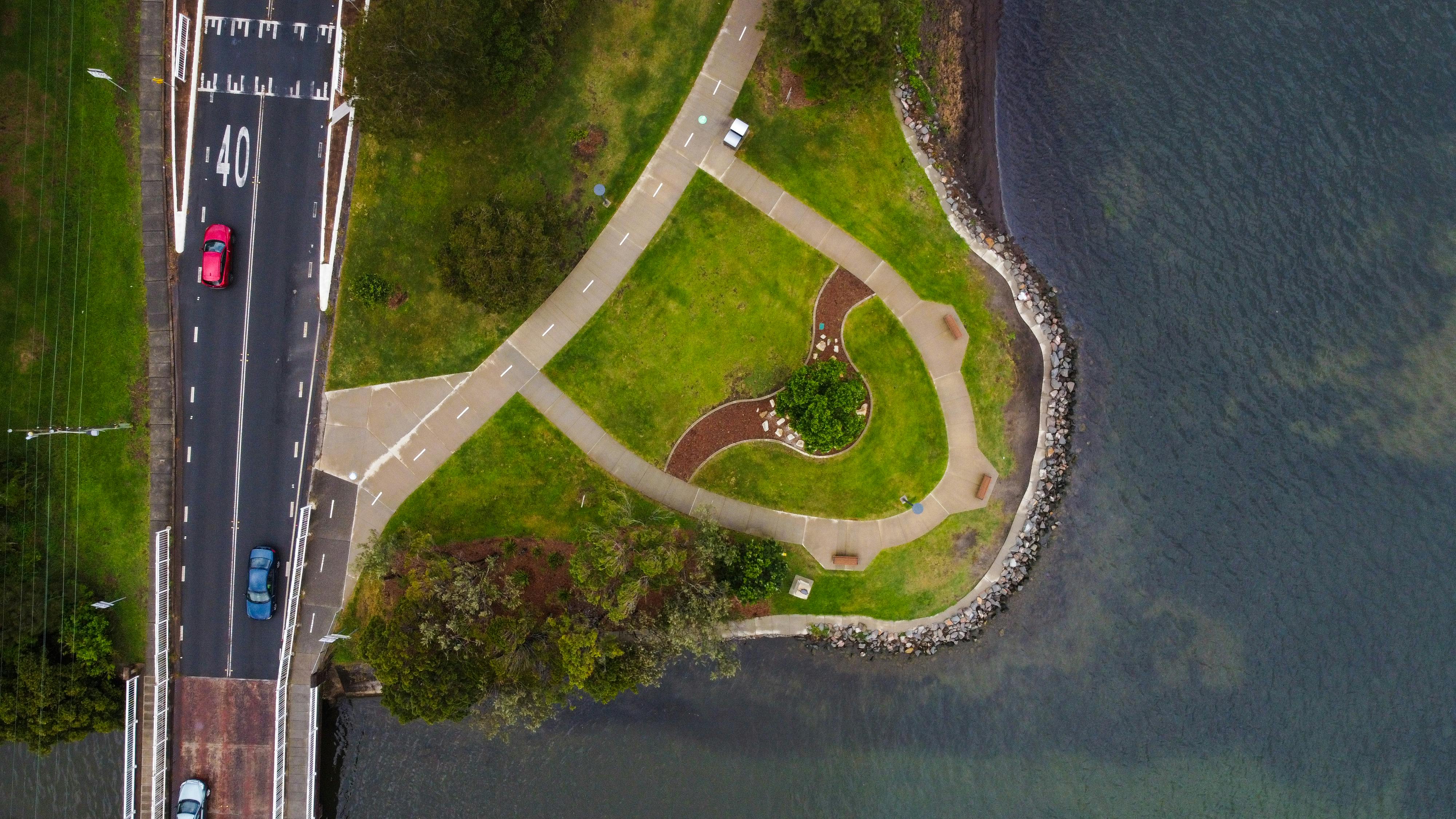 A scenic aerial view of a roadway intersecting a waterfront park with vibrant greenery.