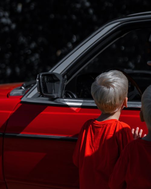 Free Two blonde boys in red shirts admiring a classic red car, mid-day outdoors. Stock Photo