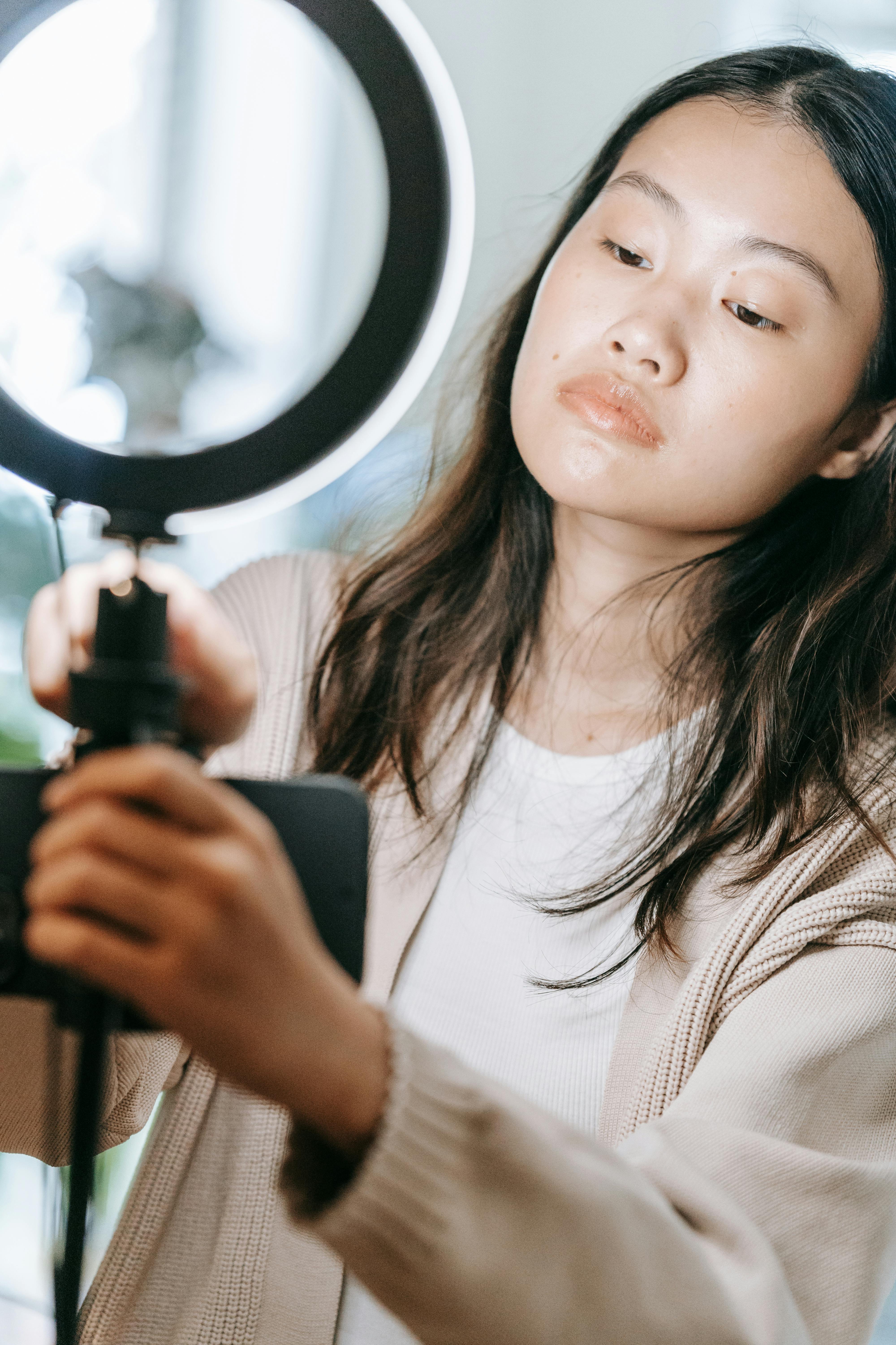 Asian woman setting up a ring light indoors, showcasing modern photography setup.