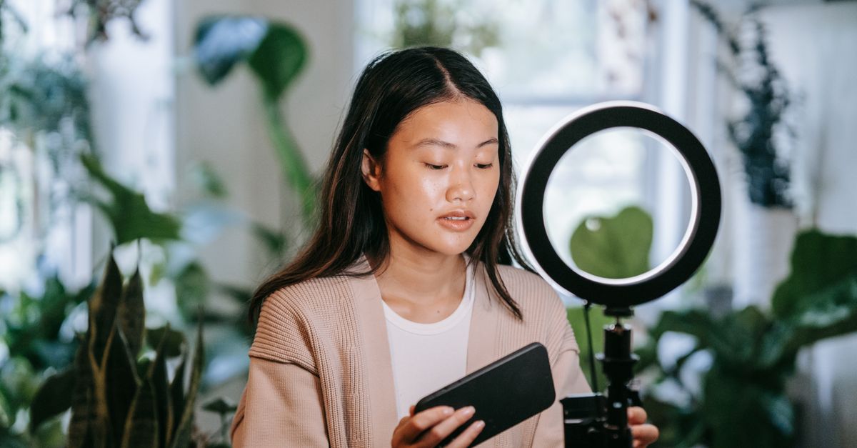 Asijská žena upravující smartphone a prstencové světlo v interiéru pro natáčení videa.