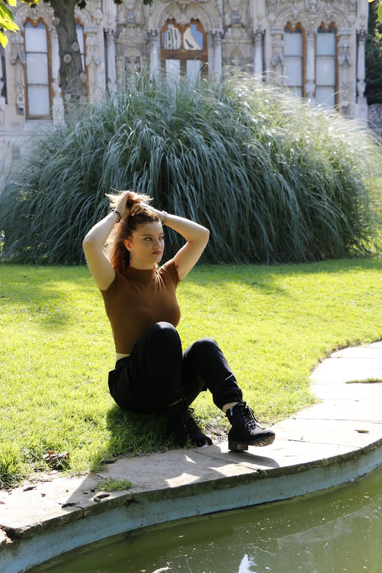 A Woman Tying Her Hair While Sitting On The Ground
