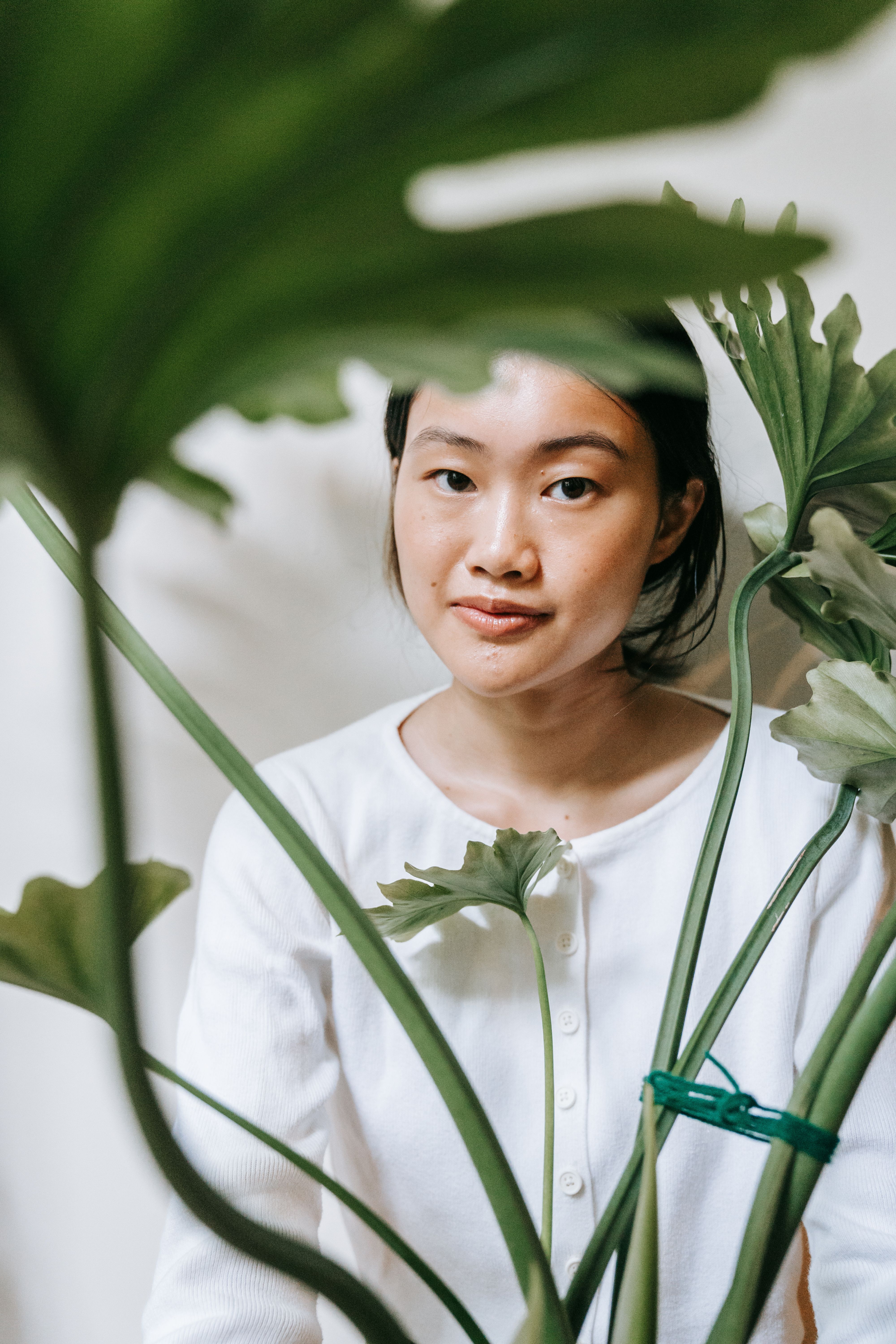 A serene portrait of a woman amidst greenery indoors, conveying calmness.