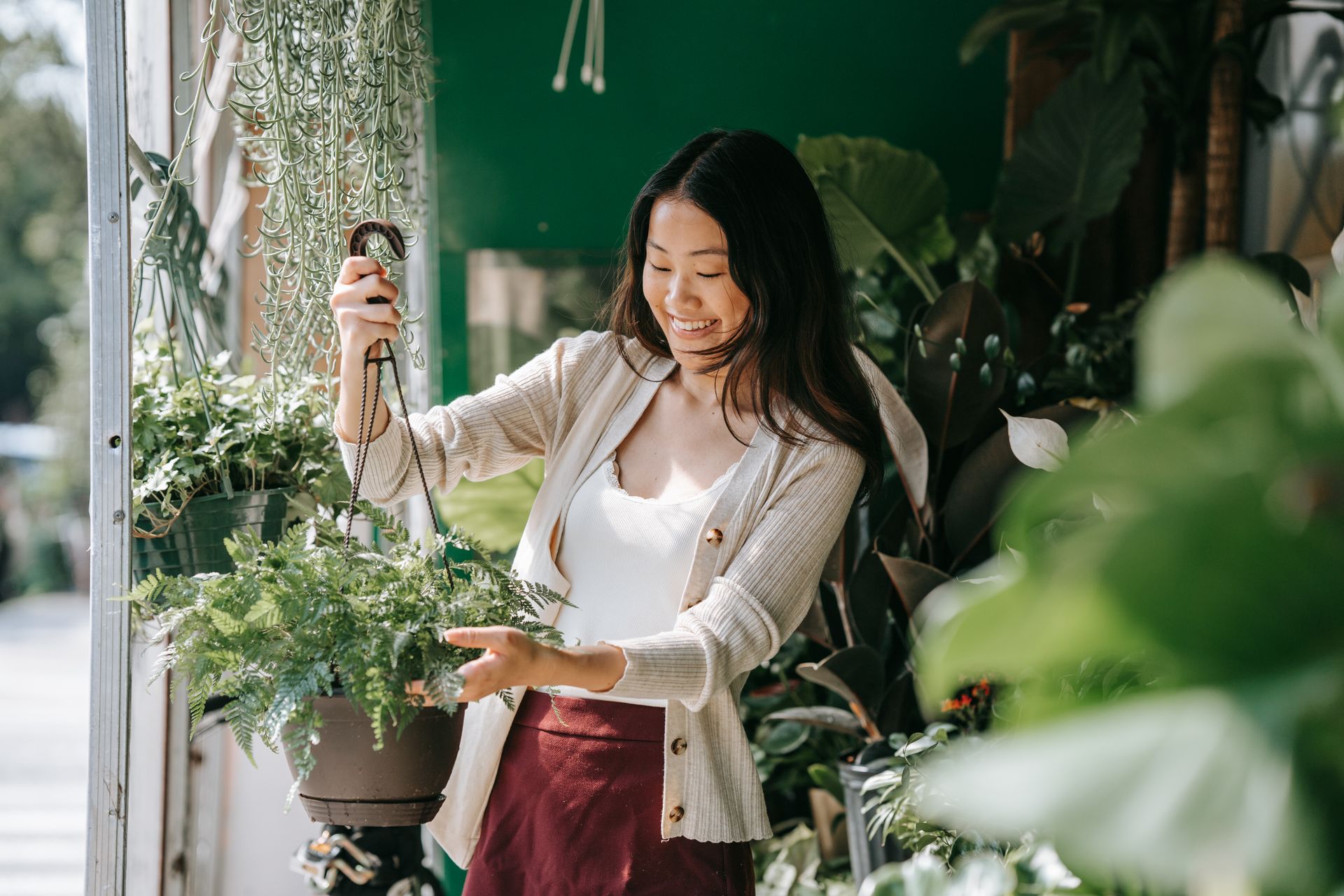 A happy Asian woman tending to indoor plants, enjoying her gardening hobby in a bright space.