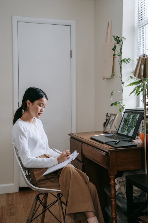 A Woman Holding a Pen and a Notebook Near a Wooden Table