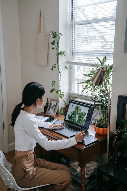 Girl in White Long Sleeves Sitting on Chair while Using Her Laptop