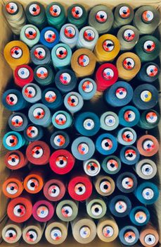 Top view of colorful spools of thread neatly arranged in a box displaying various hues.