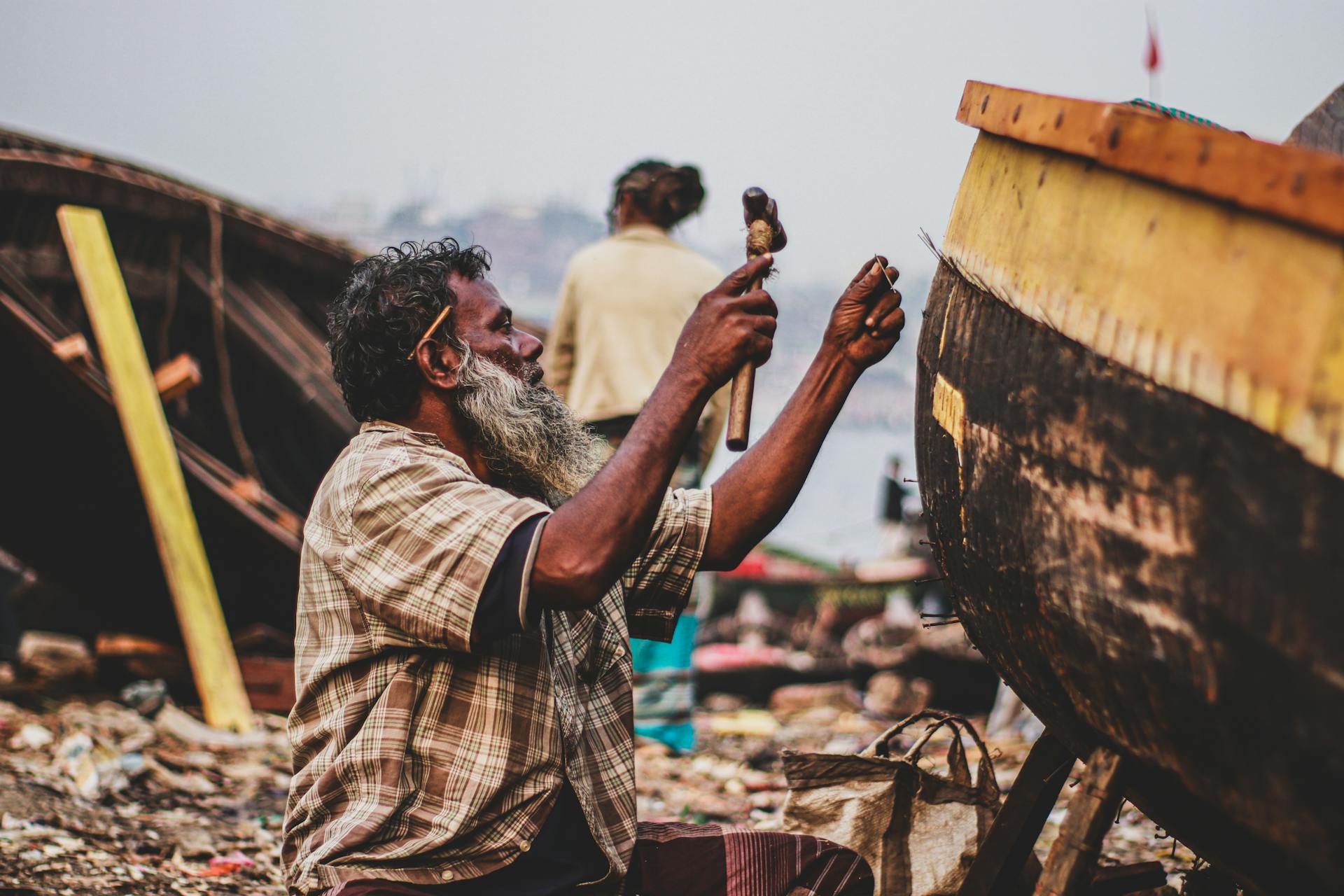 A skilled craftsman repairing a wooden boat at a boatyard on the shoreline.