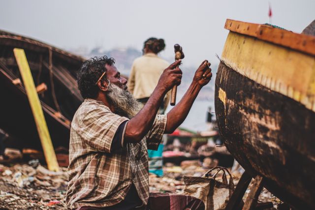 Artisan réparant un bateau en bois dans un chantier naval au bord de la mer