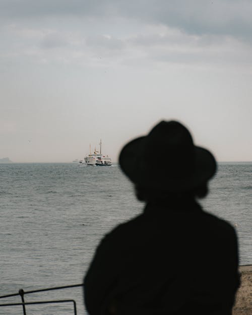 Silhouette of Person Wearing Hat Near Body of Water