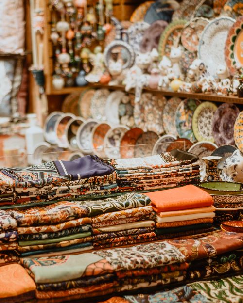 Free Vibrant display of folded textiles and ornate ceramic plates in a cozy artisan store. Stock Photo