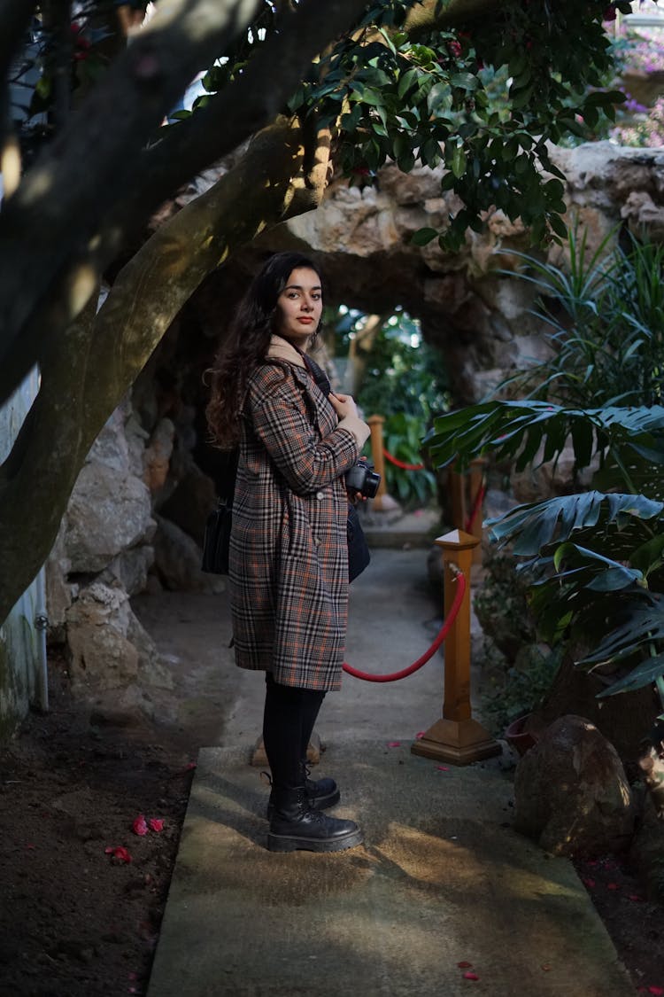 Woman In Checked Coat Standing In A Botanic Garden