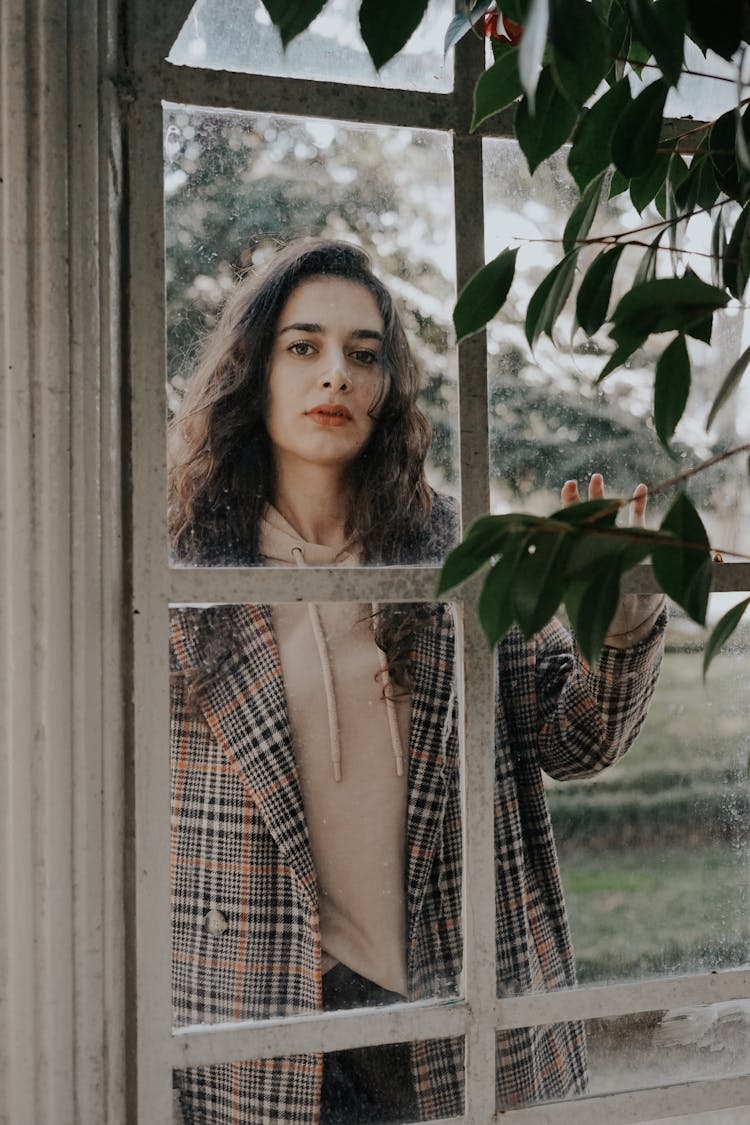 Brunette Woman Wearing A Checked Coat Looking Through Window Of Conservatory