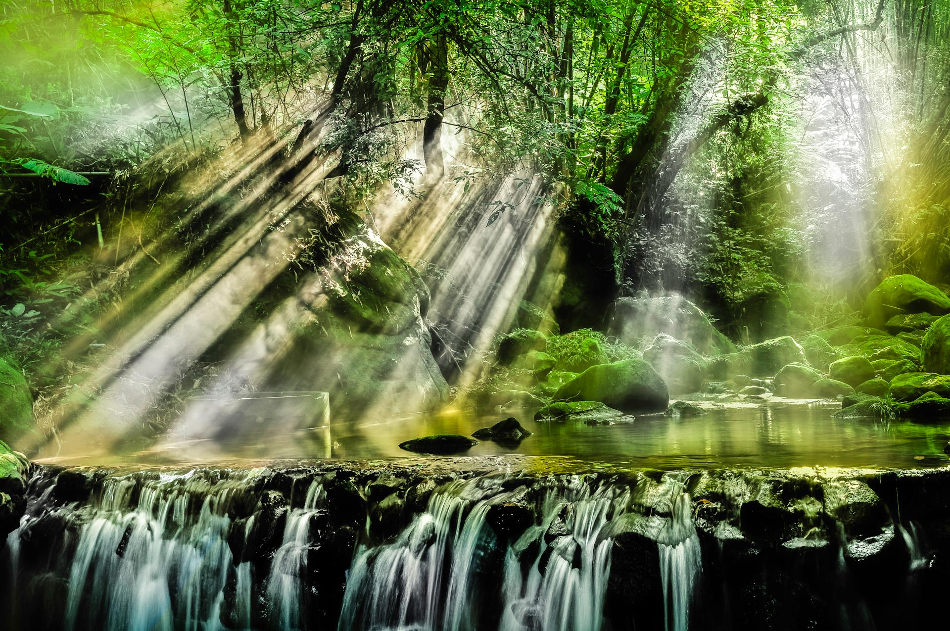 Tranquil forest scene with sunlight streaming through trees over a peaceful waterfall.