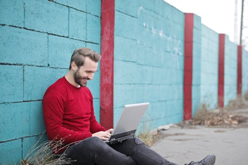 Free Man Leaning Against Wall Using Laptop Stock Photo