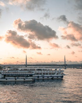 A ferry cruising near a bridge at dawn, with rippling water and a calm, scenic atmosphere.
