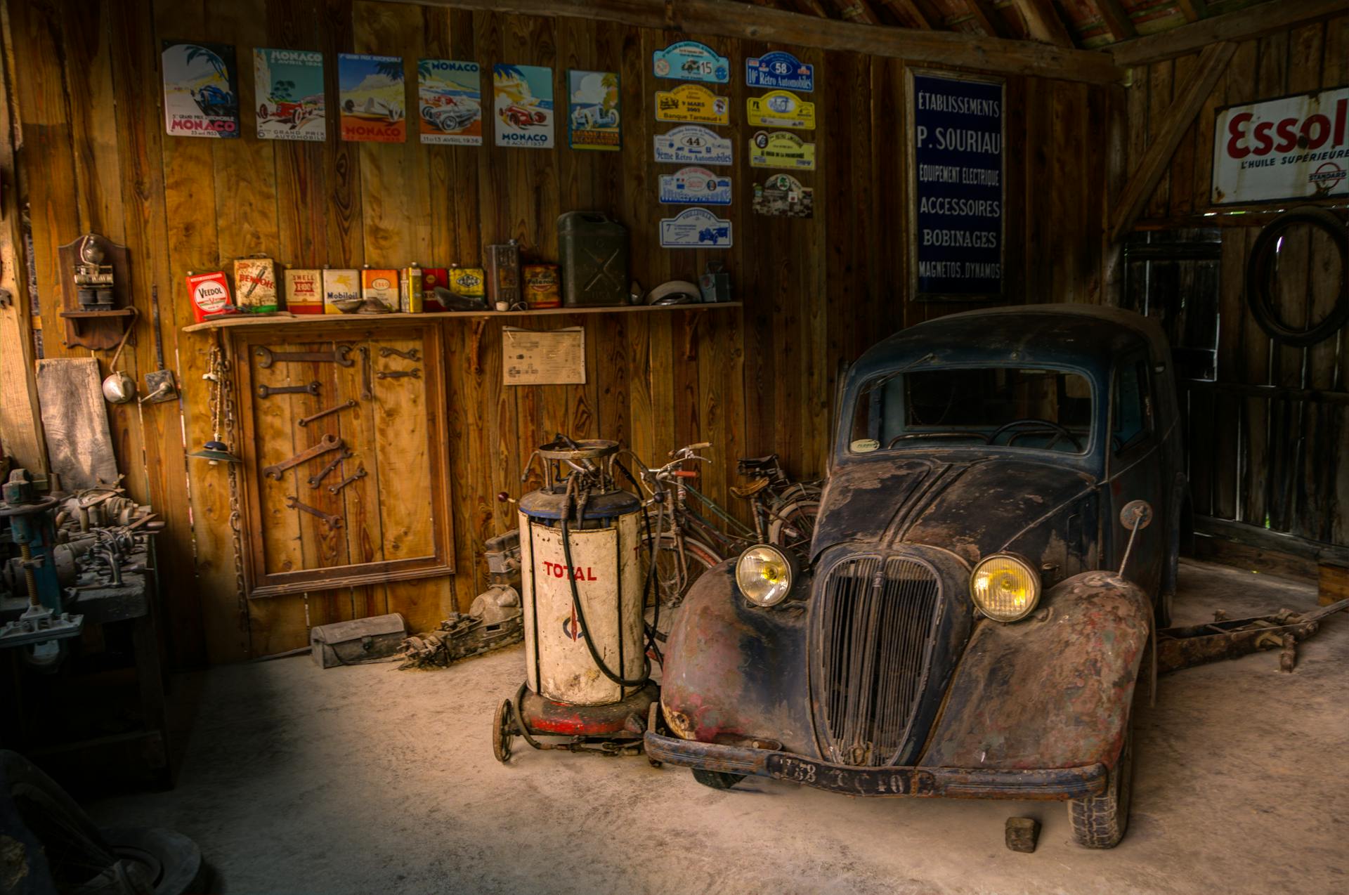 Old car in a rustic garage, surrounded by vintage signs and tools.