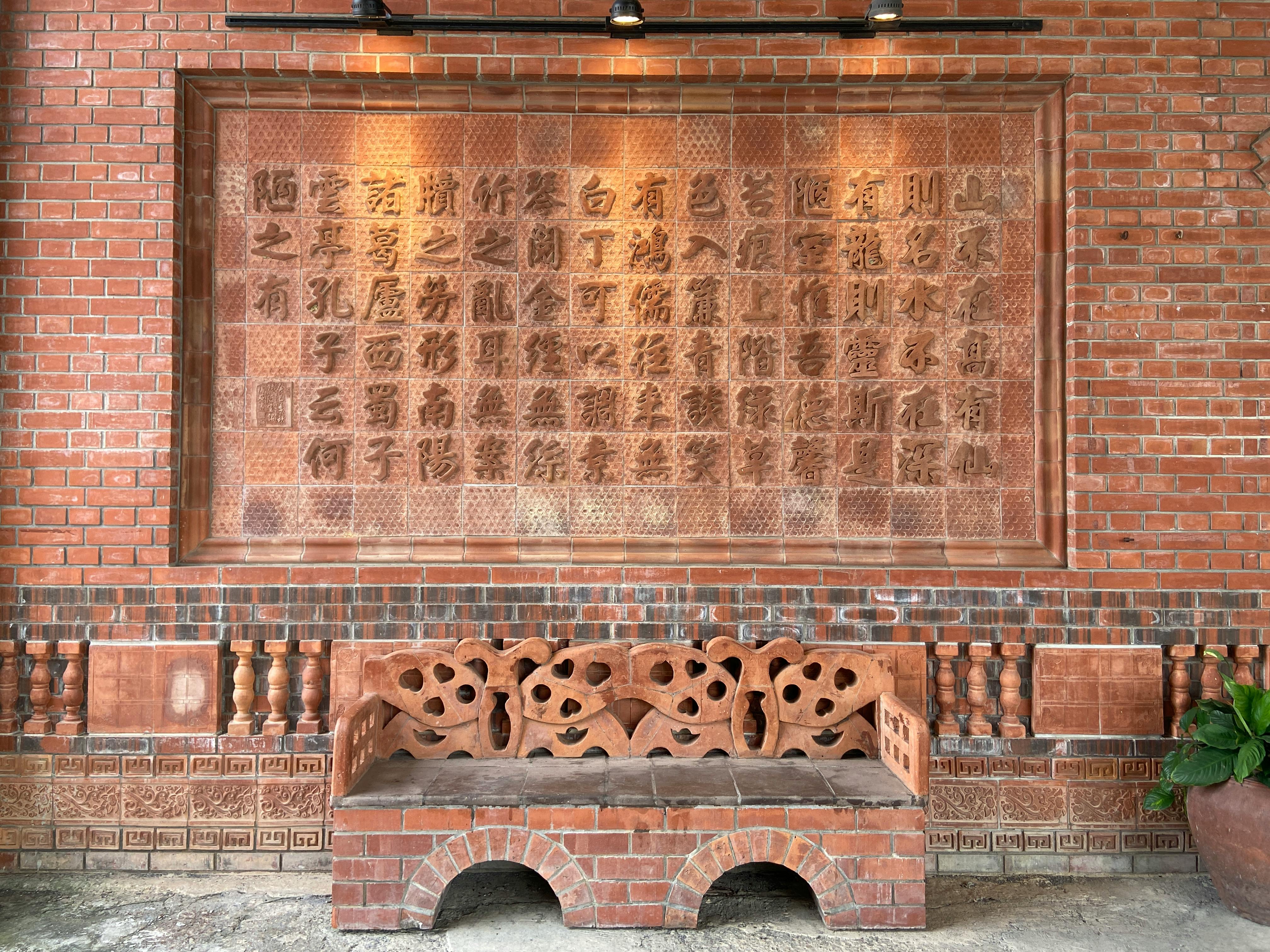Rustic brick wall featuring intricate Chinese characters and a carved bench.