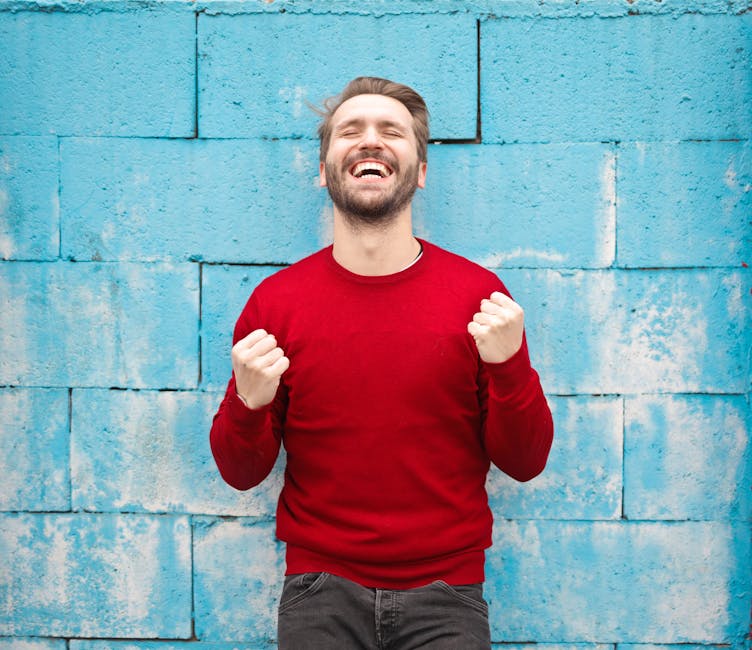 người đàn ông mặc áo len màu đỏ cười vui sướng trên nền tường màu xanh dương