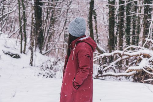 Free Person in red winter coat and grey hat standing in a snowy forest setting. Stock Photo