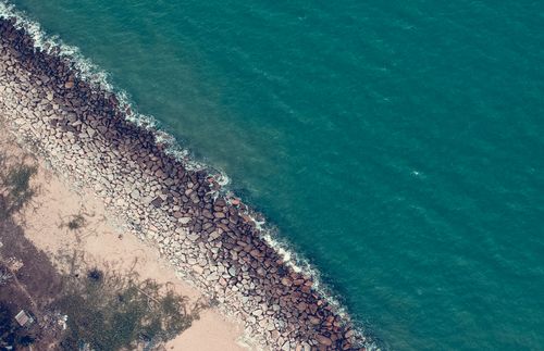 Free A scenic aerial view showcasing the rocky shoreline meeting the turquoise sea, with sandy beach visible. Stock Photo