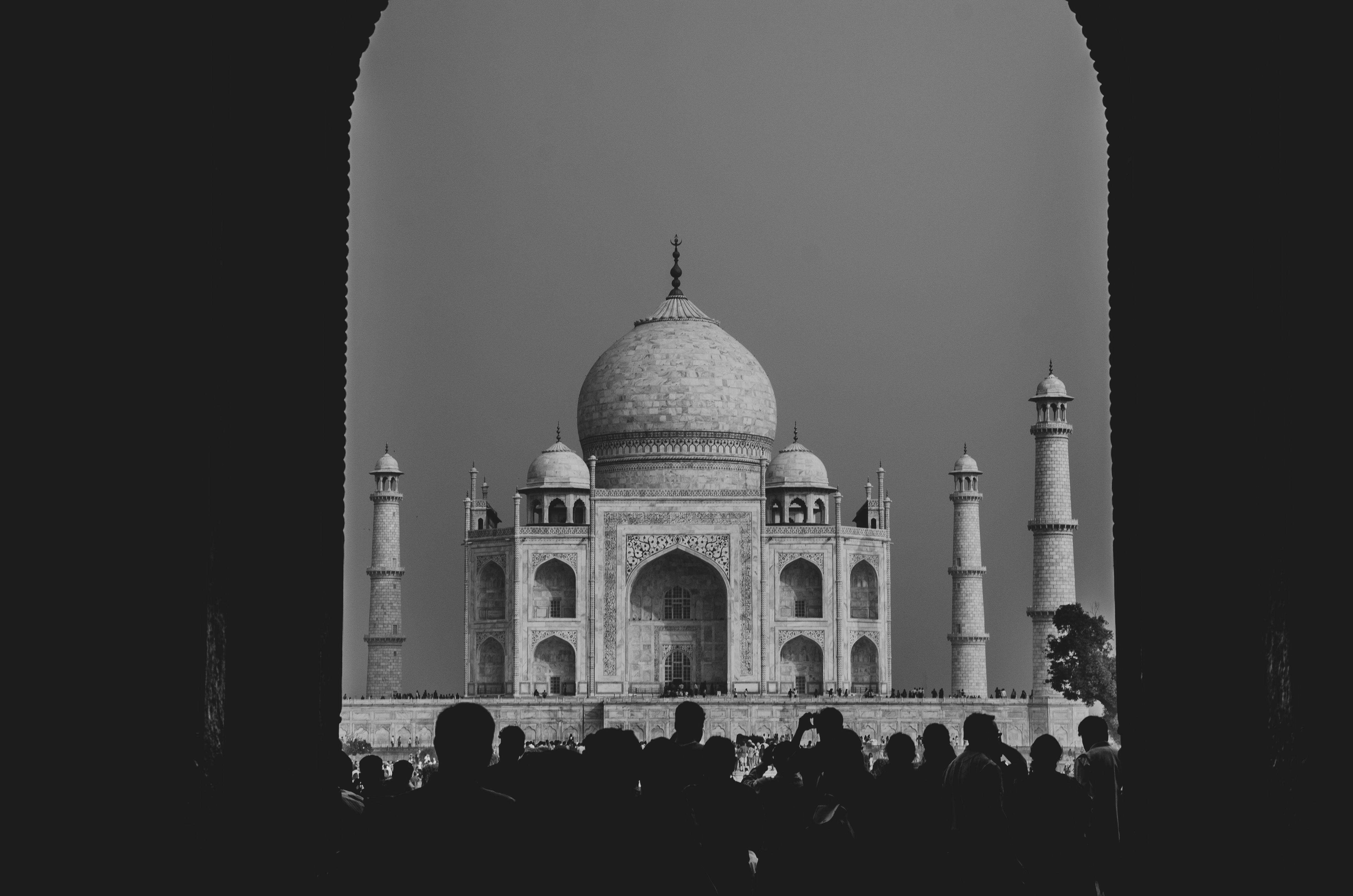 Iconic view of the Taj Mahal in black and white through an arch with silhouetted tourists.