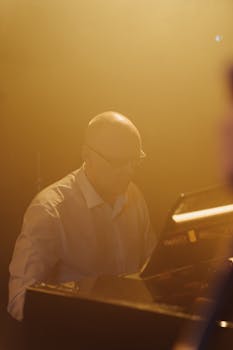 Elderly man with glasses plays piano in a warm, dim light setting creating a soothing ambiance.