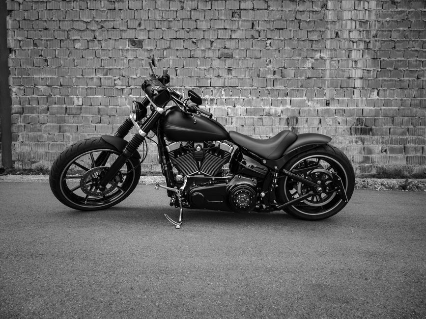 Black and white image of a motorcycle parked on the road against a brick wall.