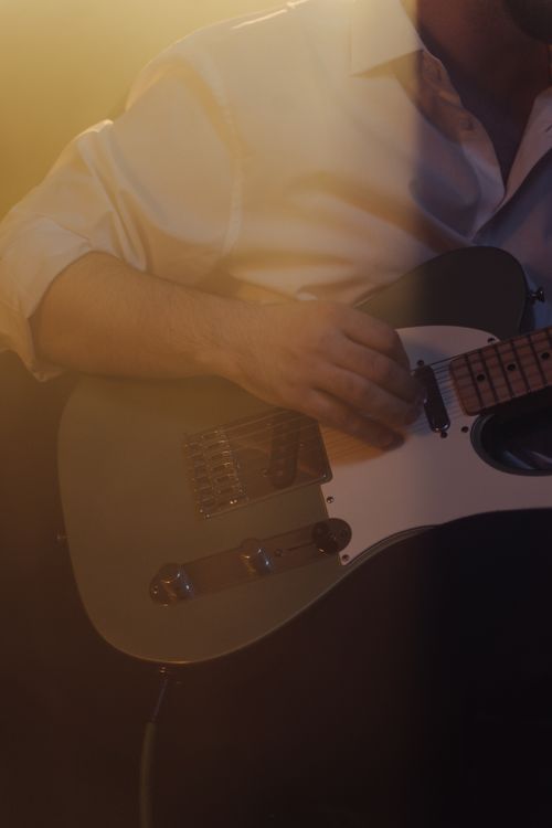 Free Musician strumming an electric guitar in warm lighting, creating a dramatic mood. Stock Photo