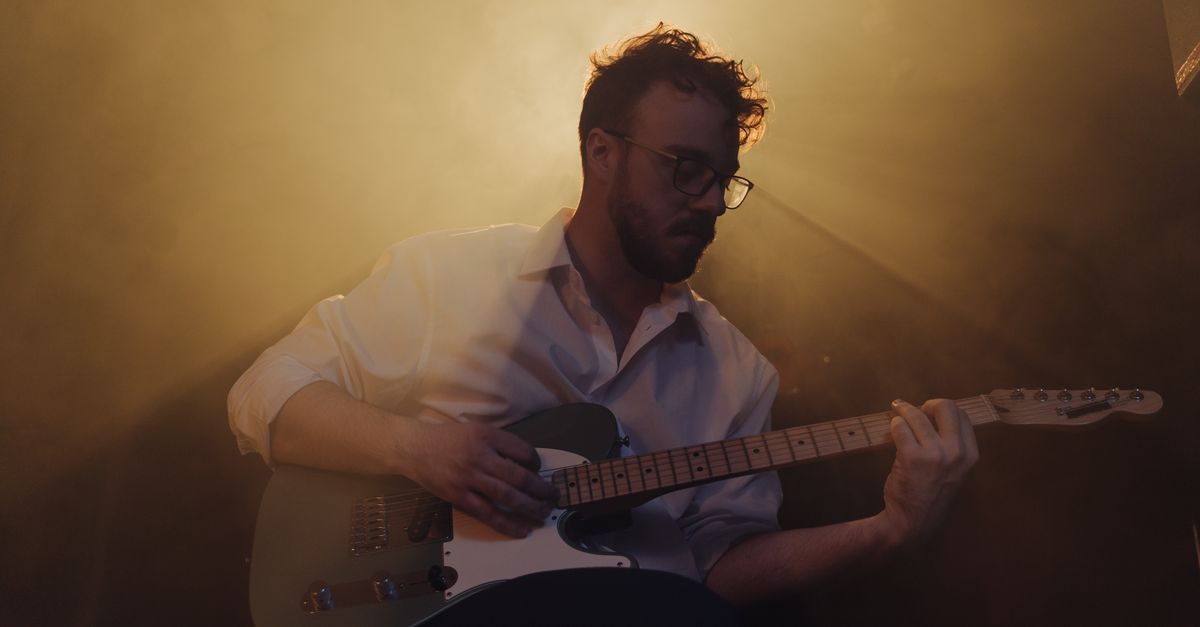a moody, cinematic photo of a musician like Kyle Cox playing guitar in a rustic setting