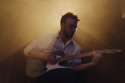 A guitarist intensely focused while playing electric guitar under dramatic stage lighting.