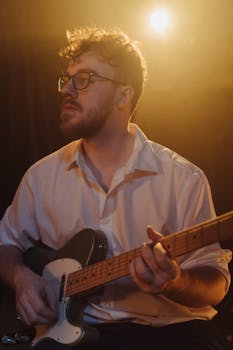 A male guitarist plays electric guitar on stage, illuminated by warm lights, creating a moody ambiance.