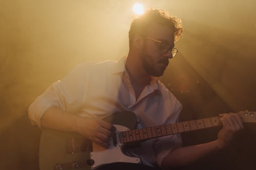 Musician playing electric guitar on stage with dramatic lighting and fog effects.