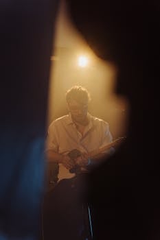 Captured moment of a guitarist focused on stage performance under warm lighting.