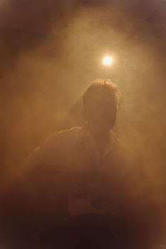 Silhouetted musician playing guitar on stage with dramatic fog and lighting.