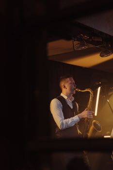 A saxophonist performing on stage under warm moody lighting, captured in a vertical shot.