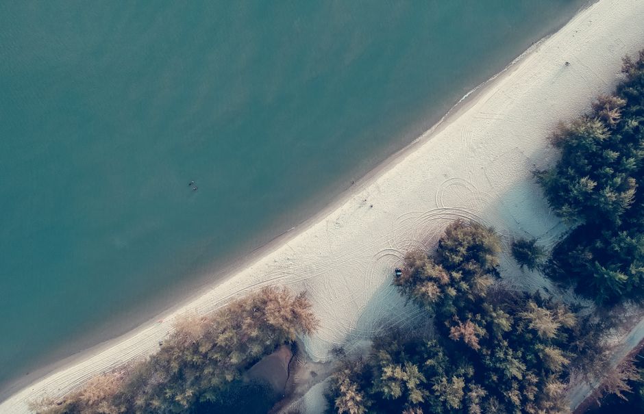 A breathtaking aerial photo capturing a tranquil beach with white sands and lush trees against a calm ocean.