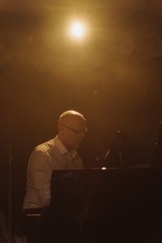 An elderly musician plays the piano in a warmly lit indoor setting, evoking a nostalgic mood.