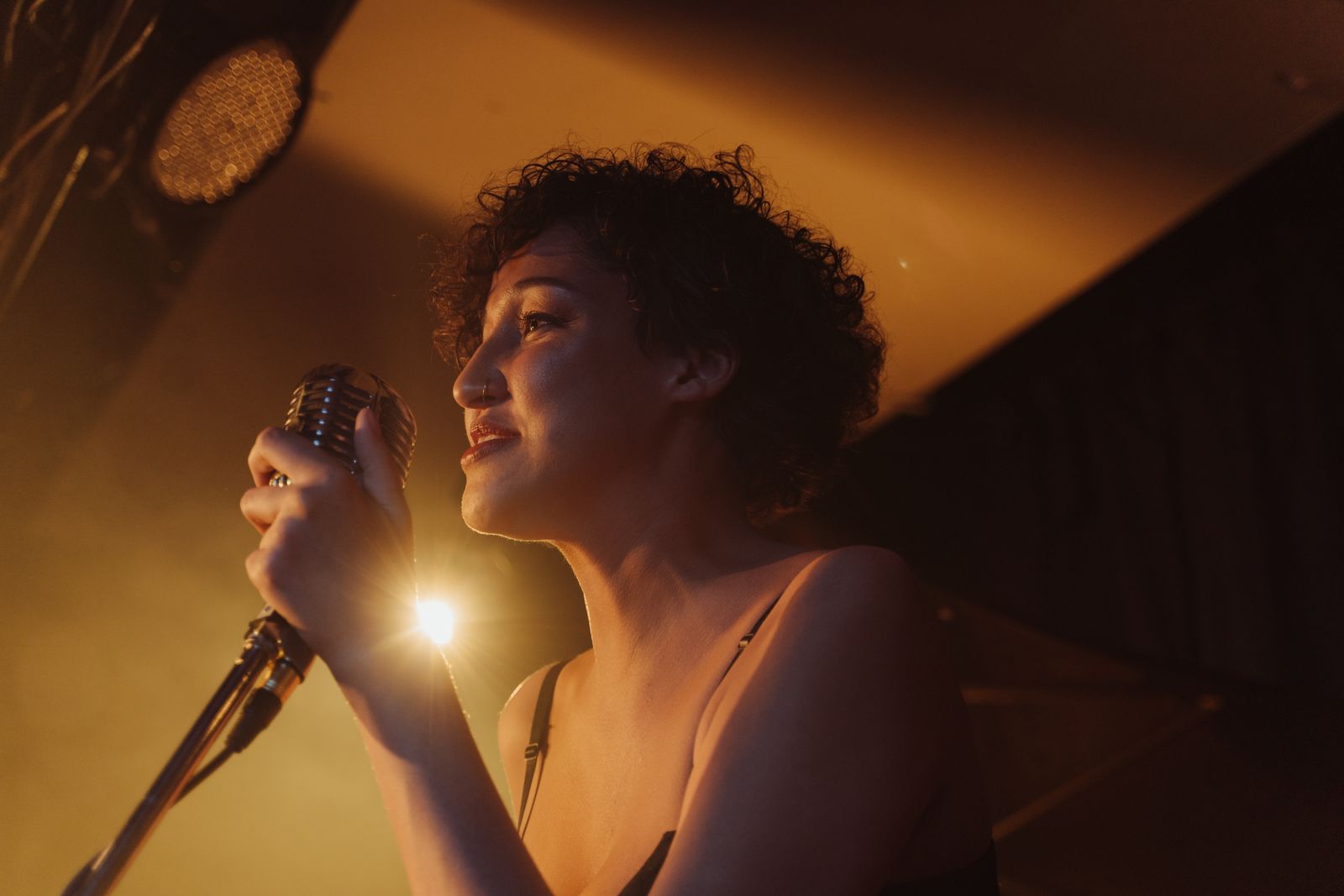 Singer performing into a vintage stage microphone under warm amber lights — photo by cottonbro studio on Pexels
