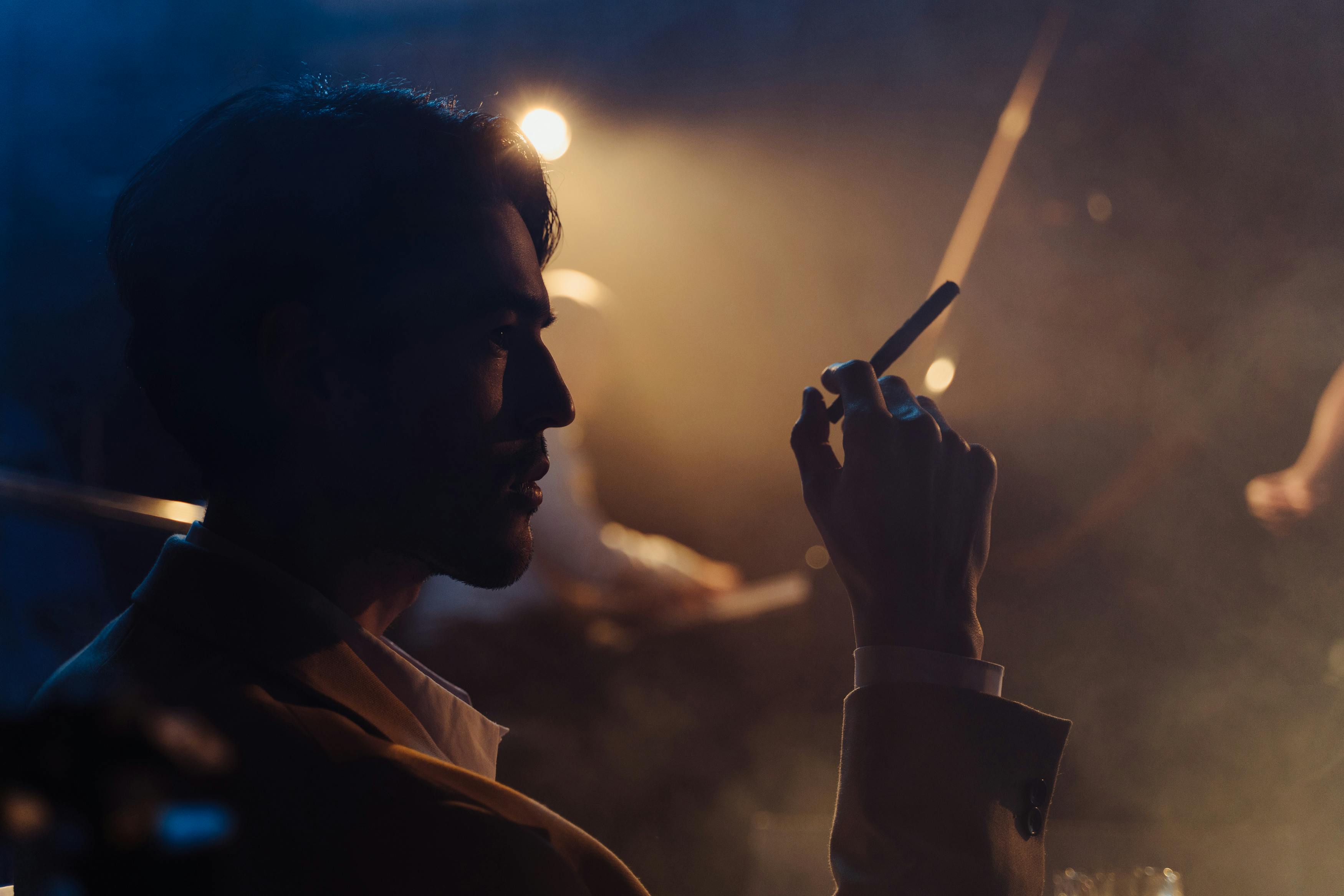 A dramatic silhouette of a man in profile smoking in a dimly lit indoor setting, exuding a moody atmosphere.