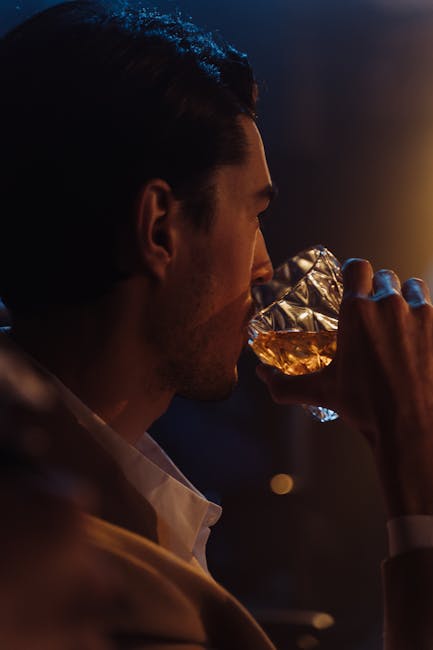 Elegant profile of a man enjoying whisky in a dimly-lit bar, showcasing mood and relaxation.