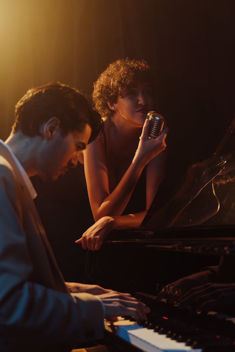 A Woman Singing While A Man Playing The Piano