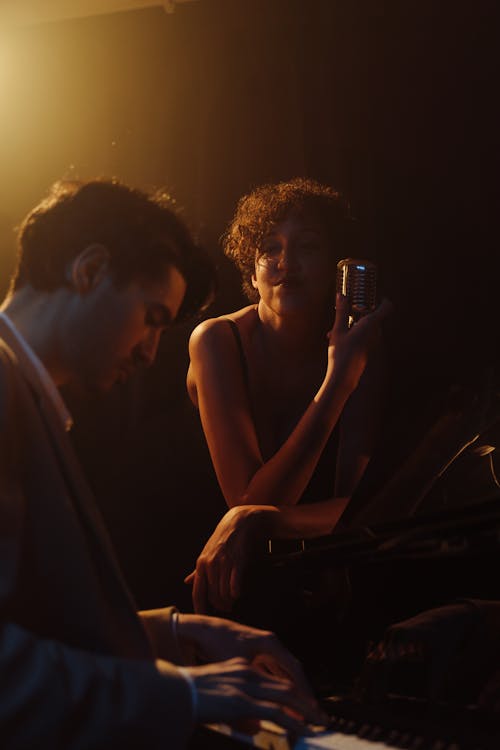 A Man Playing Piano while a Woman Holding a Microphone